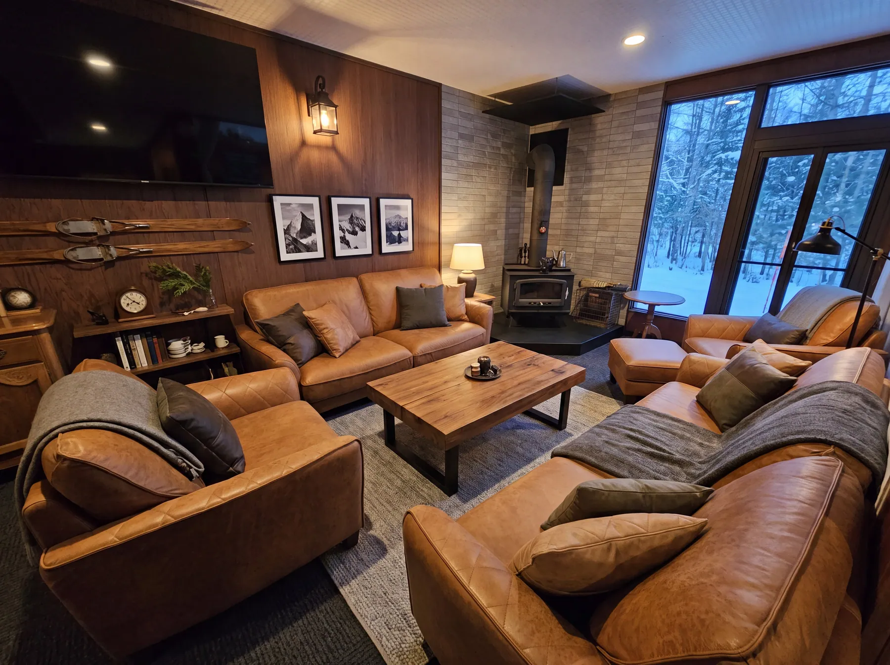 The fireside lounge: leather seating, a wood-burning stove, framed black-and-white mountain prints, snow through the window